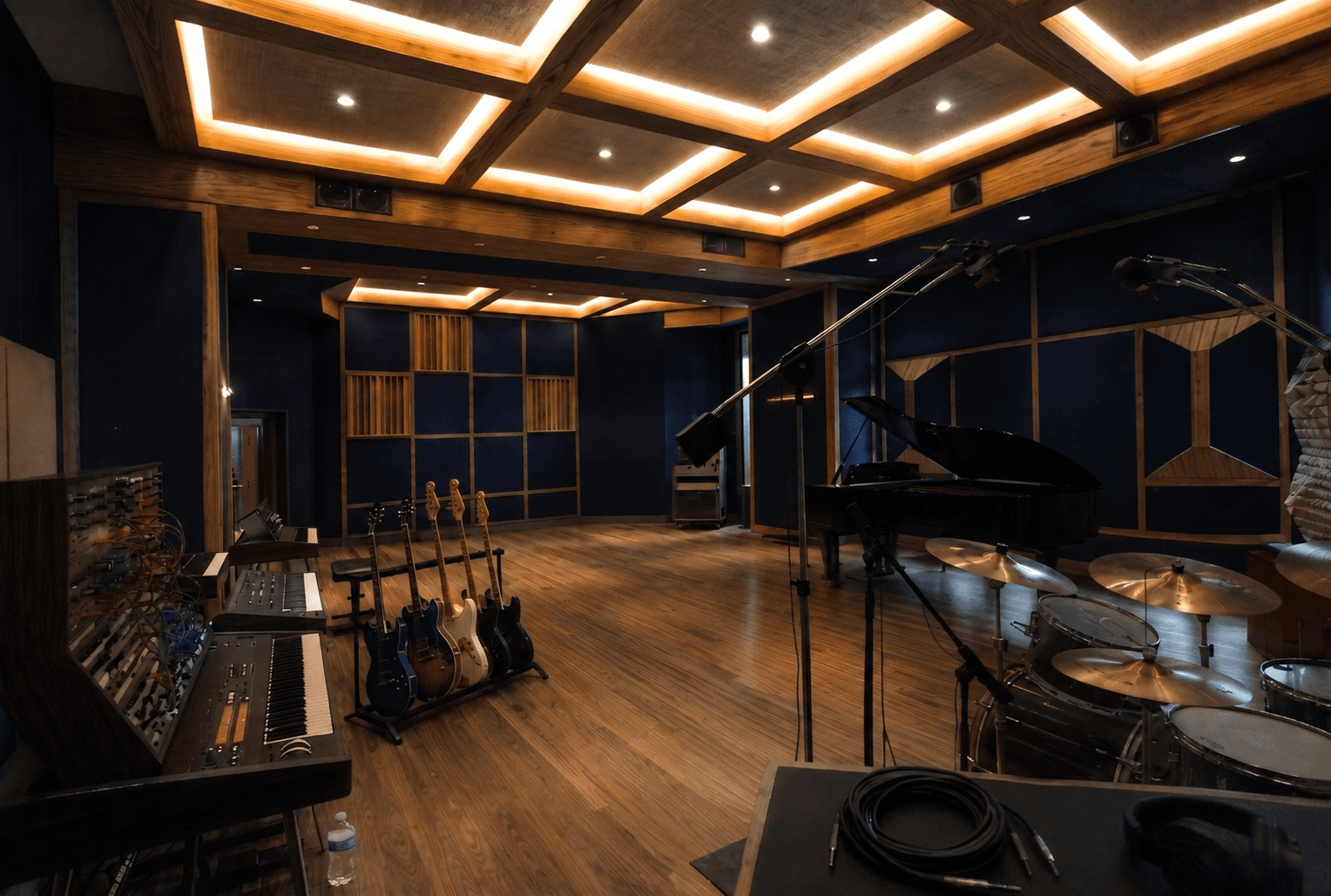 Professional recording studio featuring a grand piano, drum kit, electric guitars, and vintage synthesizers.