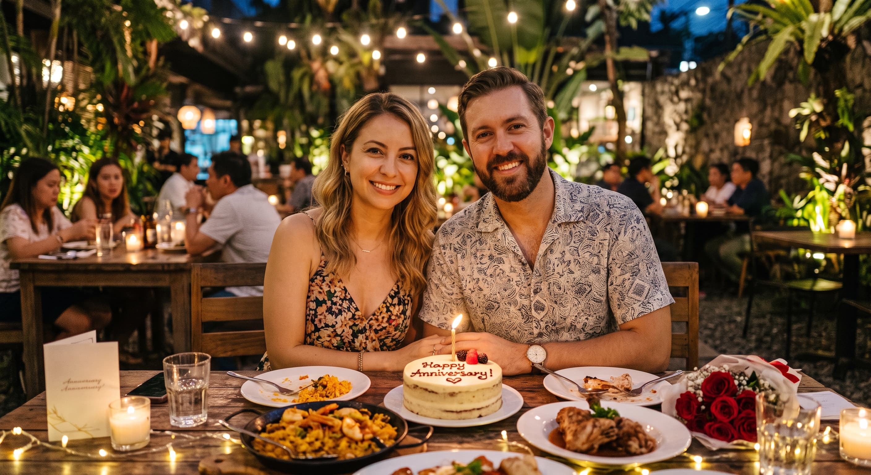 Smiling couple celebrating their anniversary with dinner, cake, and roses at a romantic outdoor restaurant.